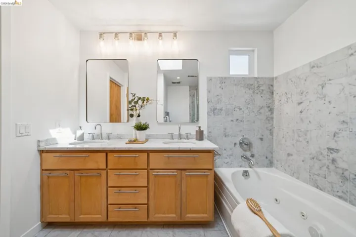 Double vanity with wood-finish cabinetry, dual rectangular mirrors, and a full-size bathtub with a tiled surround