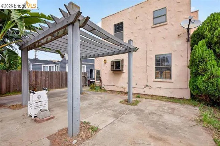 Stucco exterior with multiple windows, concrete patio, and a wood pergola