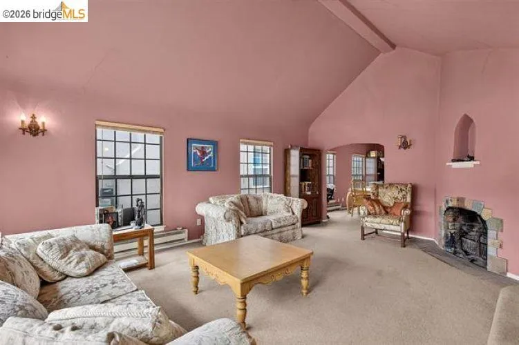 Vaulted ceiling, multiple grid windows, stone fireplace surround, wall sconces, and built-in arch niche