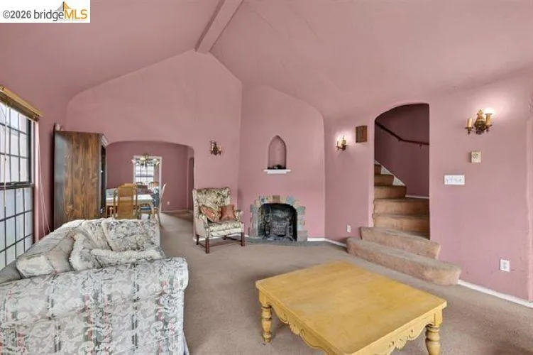 Vaulted ceiling, stone fireplace surround, arched doorways, built-in wall sconces, and interior staircase