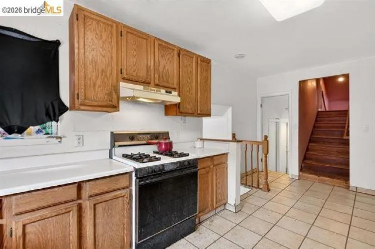 Kitchen featuring wood-finish cabinetry, white countertops, a black range, and tile flooring