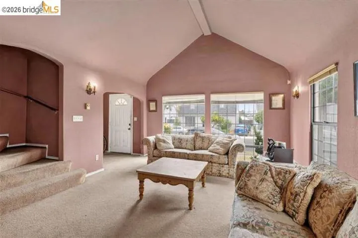 Vaulted ceiling, arched doorways, multiple windows, wall sconces, and staircase with railing