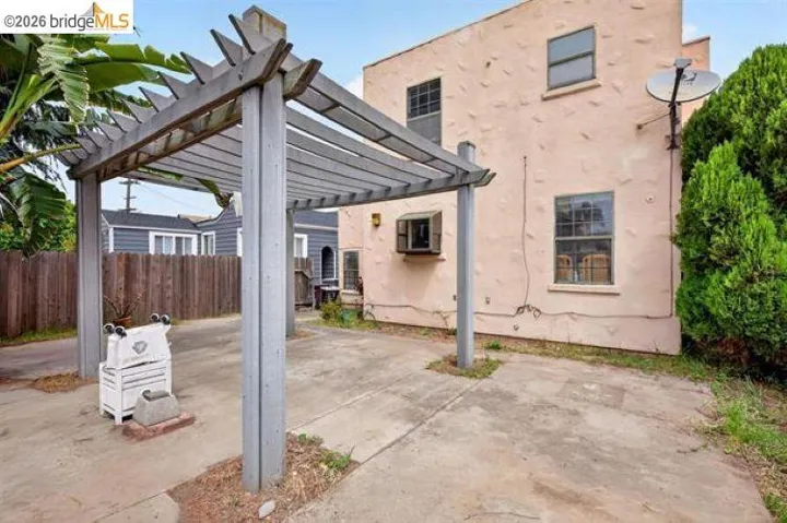Stucco exterior with multiple windows, concrete patio, and a wood pergola