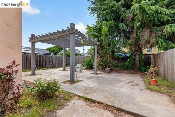 Exterior wood pergola over a concrete patio with perimeter fencing and mature trees