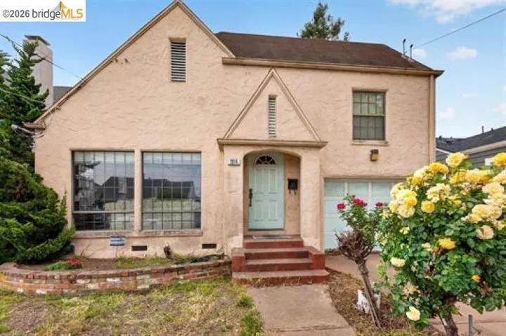 Stucco exterior with a peaked roofline, multi-pane windows, arched entry, and an integrated single-car garage