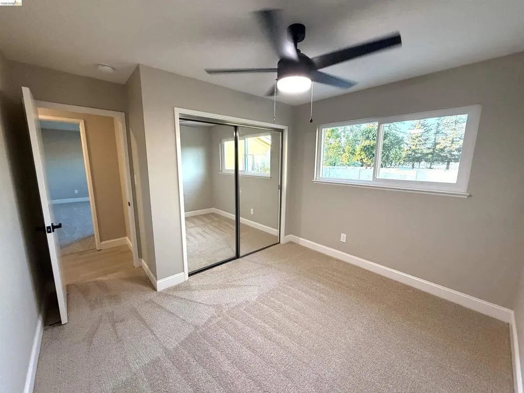 Neutral paint colors, carpet flooring, a ceiling fan with integrated lighting, a mirrored closet, and white-framed windows Neutral paint colors, carpet flooring, a ceiling fan with integrated lighting, a mirrored closet, and white-framed windows