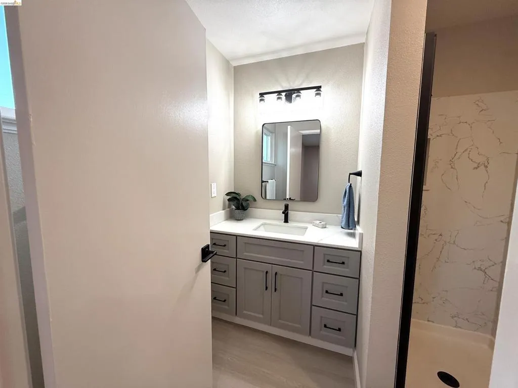 Bathroom featuring a gray vanity with shaker-style cabinetry, a white countertop, and a black-framed mirror Bathroom featuring a gray vanity with shaker-style cabinetry, a white countertop, and a black-framed mirror