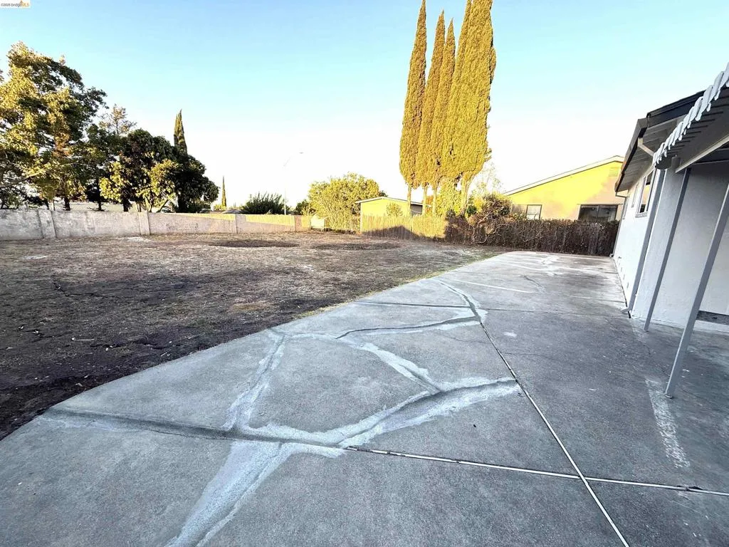 Expansive outdoor area featuring concrete paving, a private perimeter fence, and mature trees Expansive outdoor area featuring concrete paving, a private perimeter fence, and mature trees