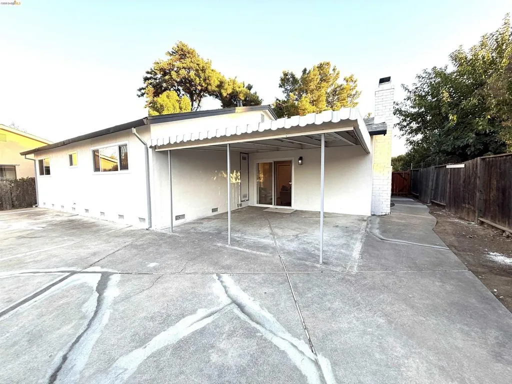 Rear exterior with an attached patio cover, sliding glass door, white stucco siding, and a brick chimney Rear exterior with an attached patio cover, sliding glass door, white stucco siding, and a brick chimney