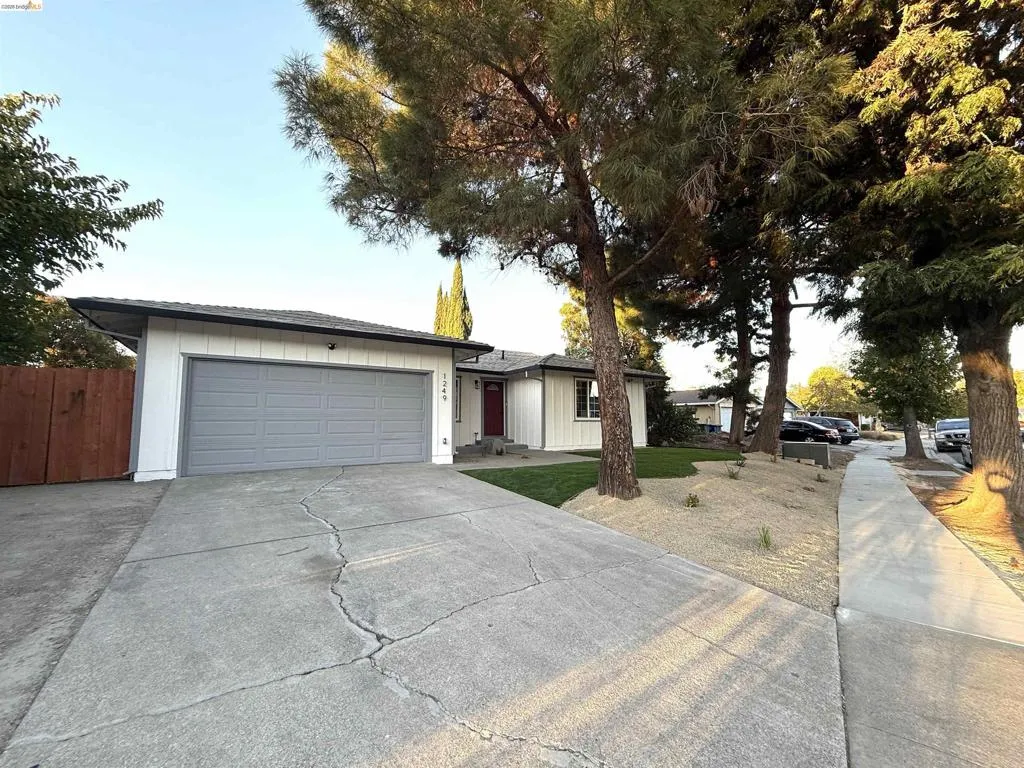 White exterior siding, gray garage door, red front door, concrete driveway, and mature landscaping White exterior siding, gray garage door, red front door, concrete driveway, and mature landscaping