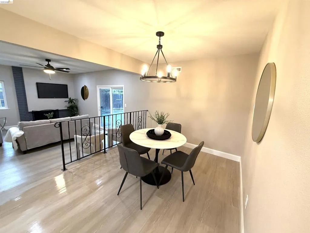 Open-concept living area with wood-finish flooring, a contemporary chandelier, and a black wrought iron railing Open-concept living area with wood-finish flooring, a contemporary chandelier, and a black wrought iron railing