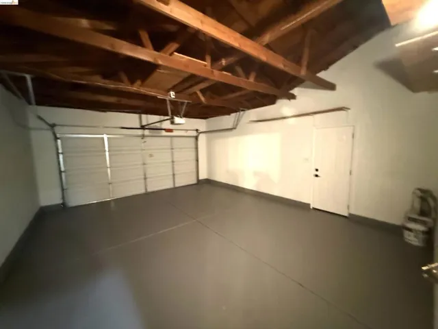Spacious garage featuring exposed beam ceiling, painted concrete flooring, and a sectional garage door
