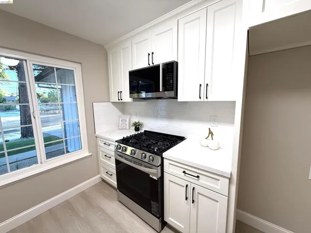 White shaker cabinetry with black hardware, stainless steel gas range, built-in microwave, white subway tile backsplash, and light-toned wood-finish flooring