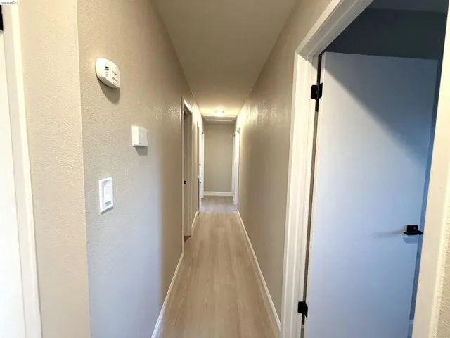 Hallway featuring light wood-finish flooring, white doors with matte black hardware, and light neutral walls