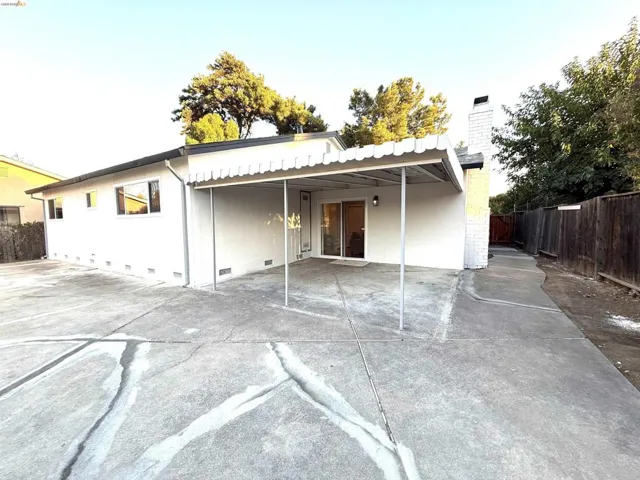 Rear exterior with an attached patio cover, sliding glass door, white stucco siding, and a brick chimney