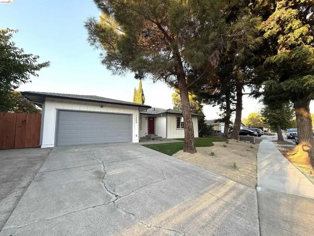 White exterior siding, gray garage door, red front door, concrete driveway, and mature landscaping