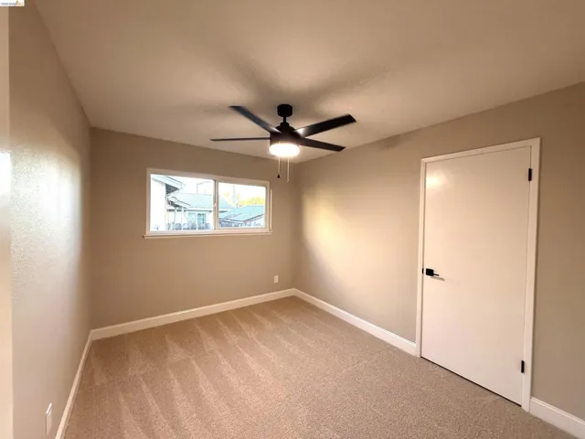 Vaulted ceiling, ceiling fan with integrated lighting, neutral-toned carpet, white trim, and a white door with matte black hardware