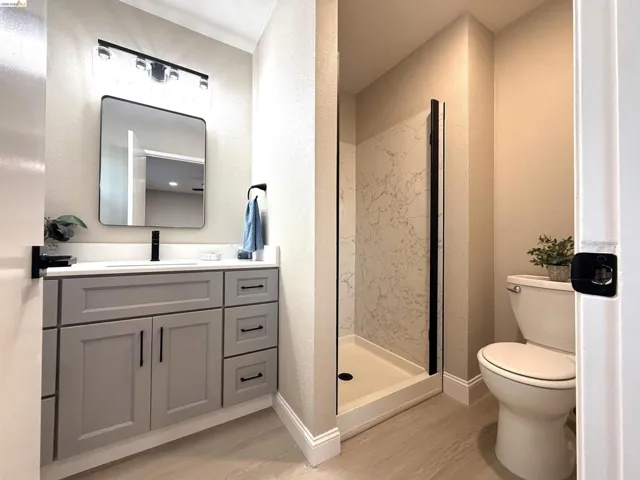Gray vanity cabinetry with black hardware, white countertop with integrated sink, black wall-mounted faucet, and a contemporary frameless mirror