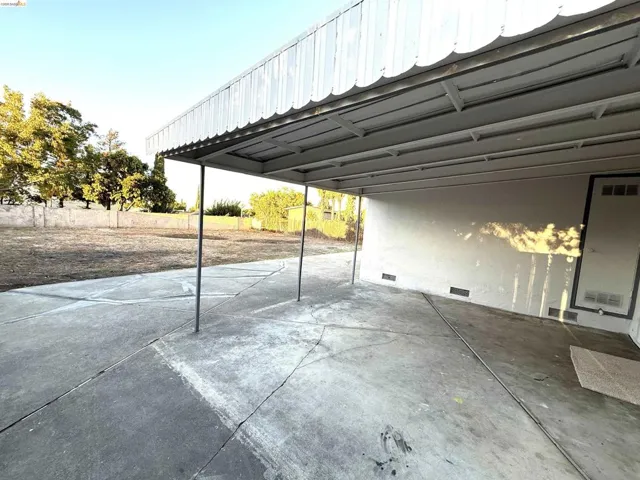 Carport with a corrugated metal roof and support posts, concrete paving, and an expansive outdoor space