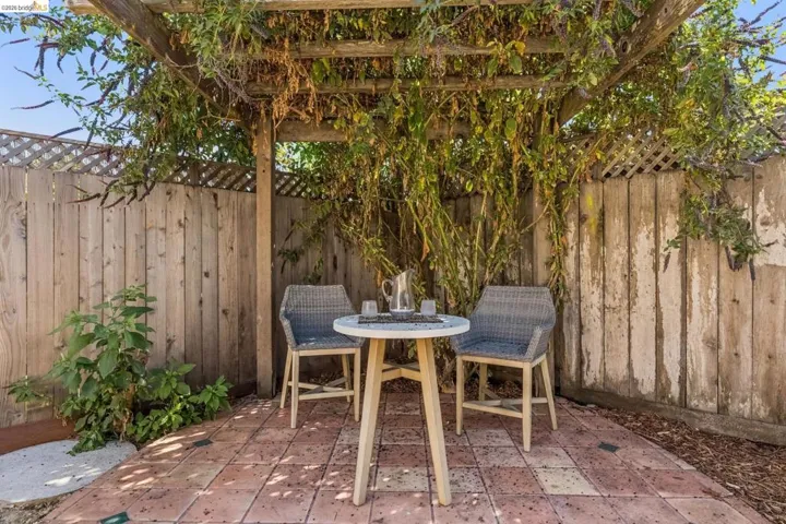 Paved patio area featuring a wooden pergola with mature climbing foliage
