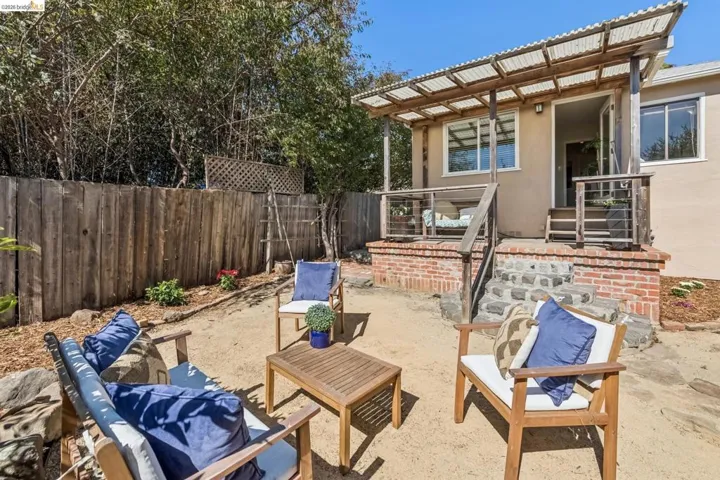 Outdoor living space featuring a wood fence, mature trees, and a covered patio with a corrugated roof