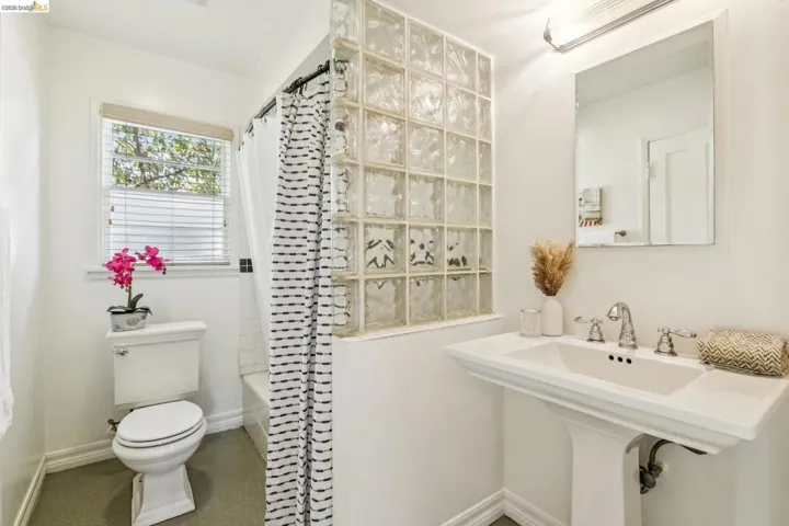 Pedestal sink, wall-mounted mirror, glass block partition, window with blinds, and a built-in bathtub with shower