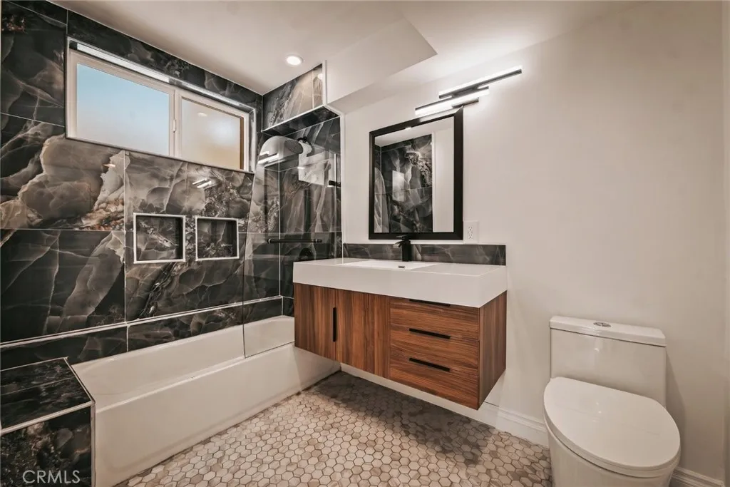 The primary suite features a walk-in closet and remodeled private bath with mosaic tile flooring, floating vanity, designer lighting, and custom-tiled tub/shower combination with glass panel. The primary suite features a walk-in closet and remodeled private bath with mosaic tile flooring, floating vanity, designer lighting, and custom-tiled tub/shower combination with glass panel.