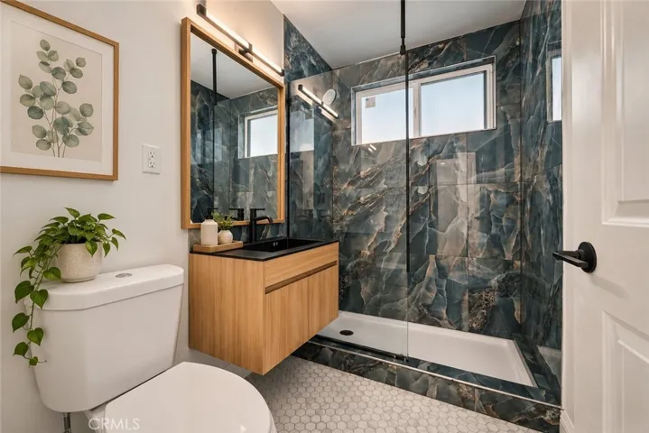 Two additional bedrooms and a beautifully remodeled secondary bath with mosaic tile flooring, floating wood vanity, black integrated trough sink, matte black fixtures, and custom-tiled step-in shower complete the bedroom wing. Photo is virtually staged.