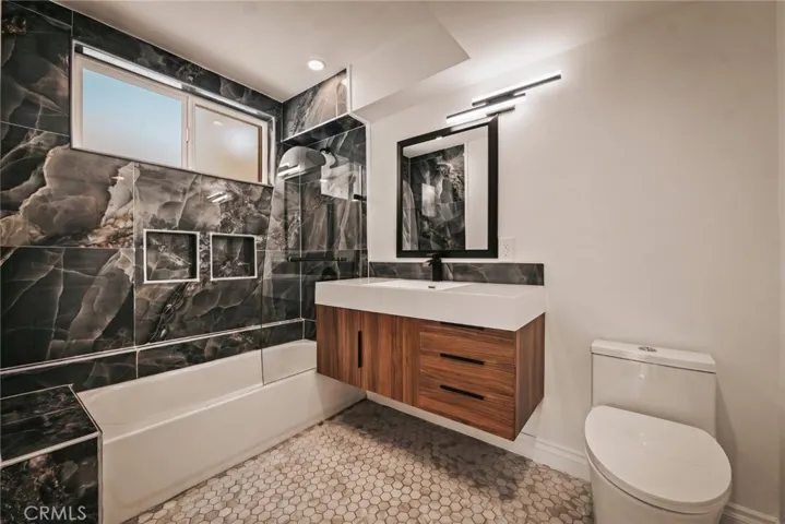 The primary suite features a walk-in closet and remodeled private bath with mosaic tile flooring, floating vanity, designer lighting, and custom-tiled tub/shower combination with glass panel.