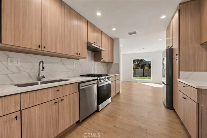 The remodeled kitchen features contemporary soft-close cabinetry, stone countertops, stainless steel refrigerator, gas range and dishwasher, an undermount sink, and pantry storage.