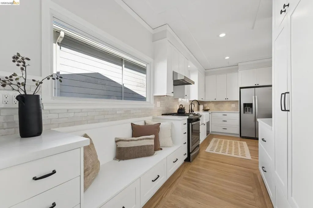 Kitchen featuring white Shaker-style cabinetry, built-in bench seating with storage drawers, light-toned wood-finish flooring, subway tile backsplash, and stainless steel appliances