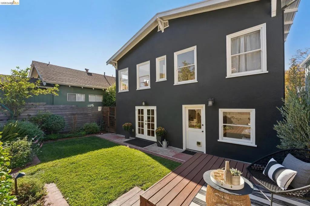 Two-story exterior featuring dark-toned stucco, wood-finish decking, double glass-panel doors, and a landscaped lawn with brick pathways