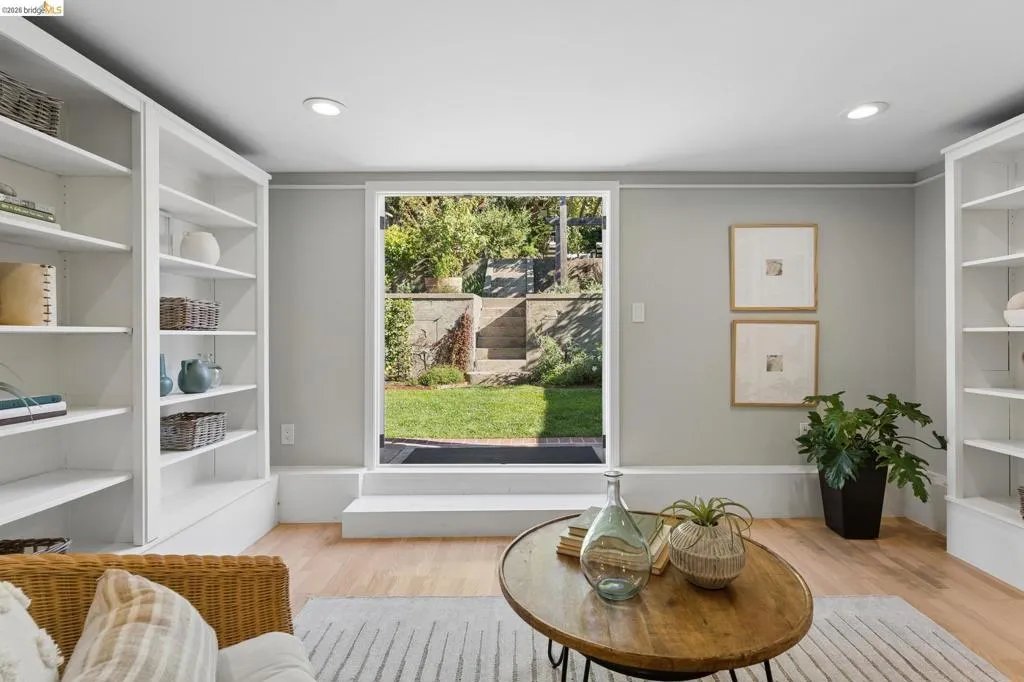 Built-in floor-to-ceiling shelving, light-toned wood flooring, recessed lighting, and a glass-paneled exterior door opening to a terraced stone landscape