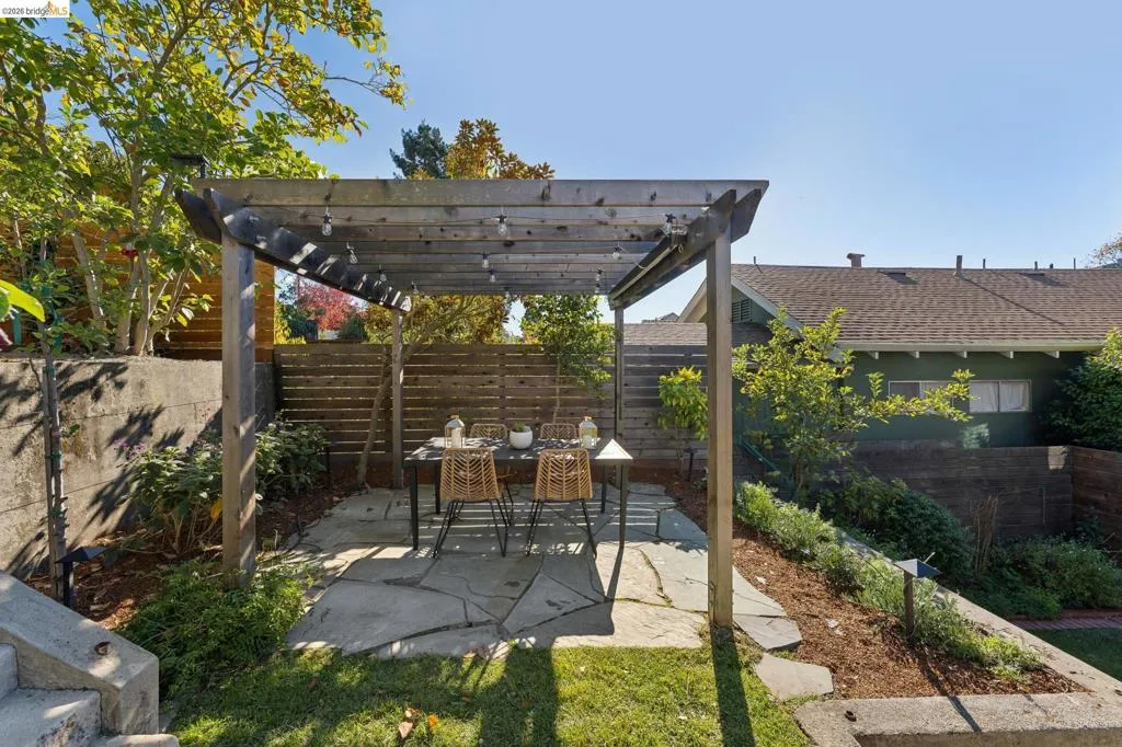 Backyard outdoor area featuring a wood-beam pergola, natural stone flagstone patio, horizontal wood slat privacy fencing, and concrete retaining walls