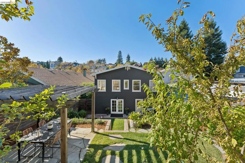Rear exterior featuring dark-toned siding, a wooden pergola, stone patio, grass lawn, and multiple windows with white trim