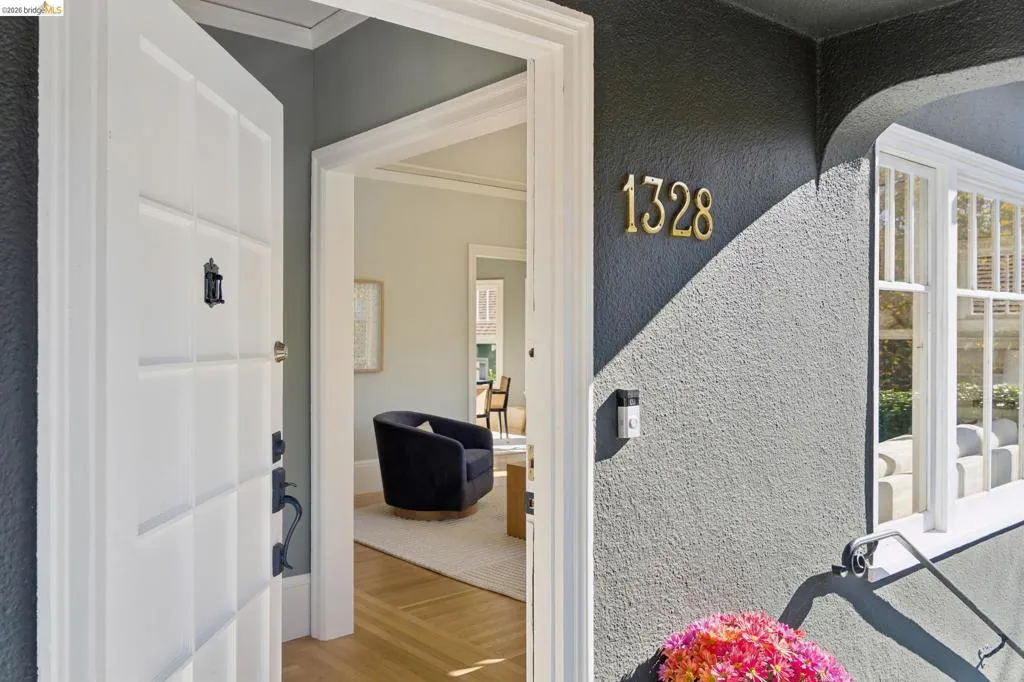 Entryway featuring a multi-paneled white door, gold-finish house numbers, textured charcoal exterior siding, and wood-finish flooring