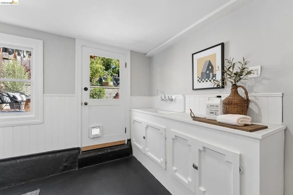 Utility space featuring white wainscoting, painted concrete flooring, custom built-in cabinetry, an integrated sink with a wall-mounted faucet, and a paneled exterior door