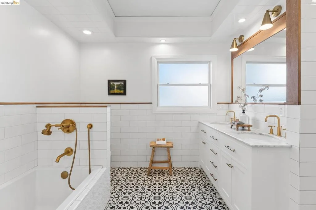Bathroom featuring patterned tile flooring, white subway tile wall treatments, a white dual-sink vanity with stone countertop, brass finish fixtures, and a recessed ceiling