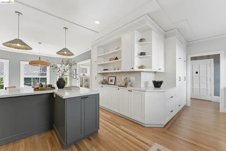 Custom cabinetry with open shelving, integrated pantry storage, wood-finish flooring, stone countertops, and three tiered pendant lights