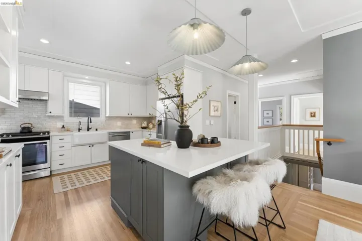 Kitchen featuring a center island with a stone-surface countertop, white cabinetry, farmhouse-style sink, stainless steel appliances, and wood-finish flooring