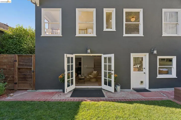 Exterior rear facade featuring smooth dark-toned stucco, white-framed multi-pane French doors, a manicured lawn, and a brick-bordered concrete patio