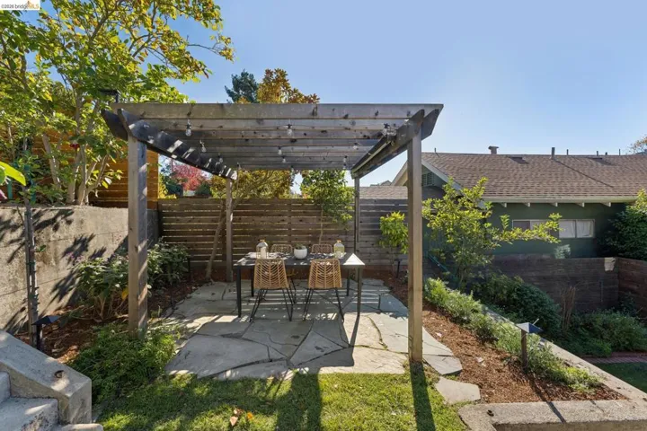 Backyard outdoor area featuring a wood-beam pergola, natural stone flagstone patio, horizontal wood slat privacy fencing, and concrete retaining walls
