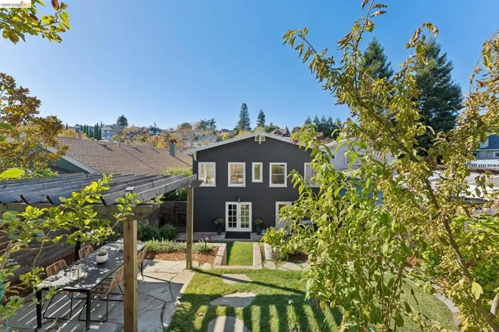 Rear exterior featuring dark-toned siding, a wooden pergola, stone patio, grass lawn, and multiple windows with white trim