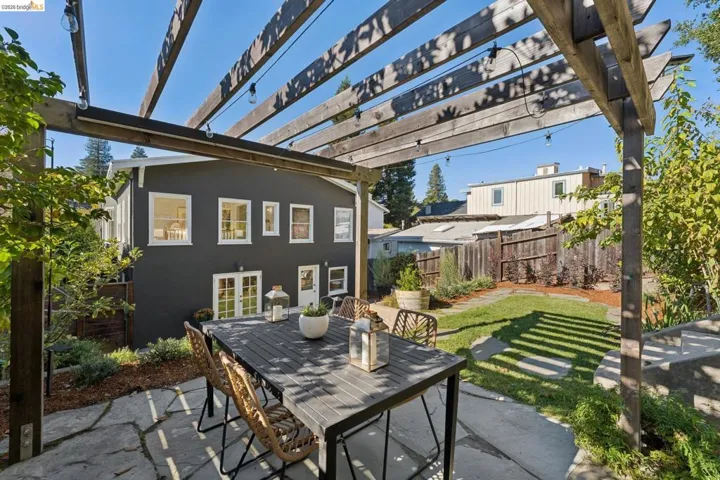Rear exterior space featuring a wood pergola, flagstone patio, manicured lawn, and mature landscaping