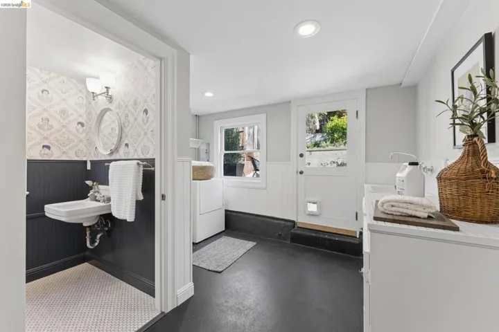 Utility space featuring dark painted wainscoting, patterned wallpaper, wall-mounted sink, recessed lighting, and a single-light door