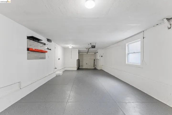 Garage interior featuring a gray epoxy-coated floor, white painted walls, single-pane window, and an automated overhead door opener