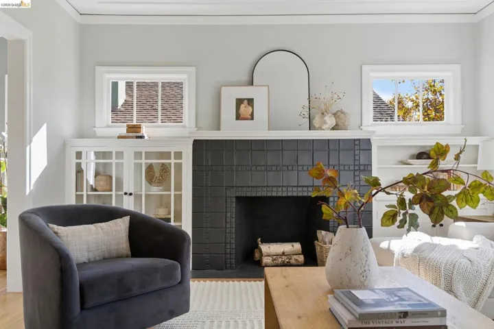 Fireplace featuring a matte black square-tiled surround, tiered white mantel, recessed built-in shelving with glass-front cabinets, and dual horizontal windows