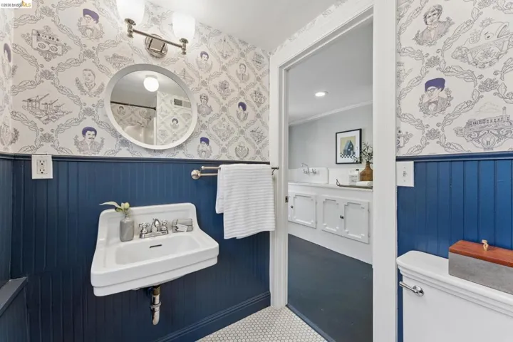 Bathroom featuring blue wainscoting, wall-mounted porcelain sink, round mirror, two-light fixture, and hexagonal floor tiling