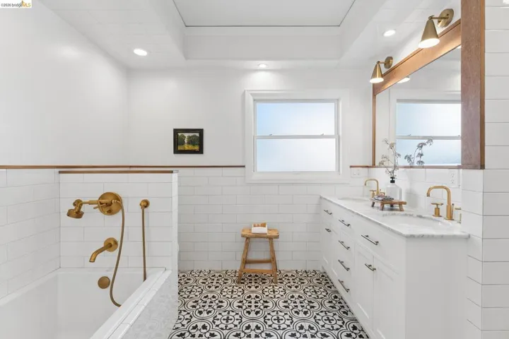 Bathroom featuring patterned tile flooring, white subway tile wall treatments, a white dual-sink vanity with stone countertop, brass finish fixtures, and a recessed ceiling