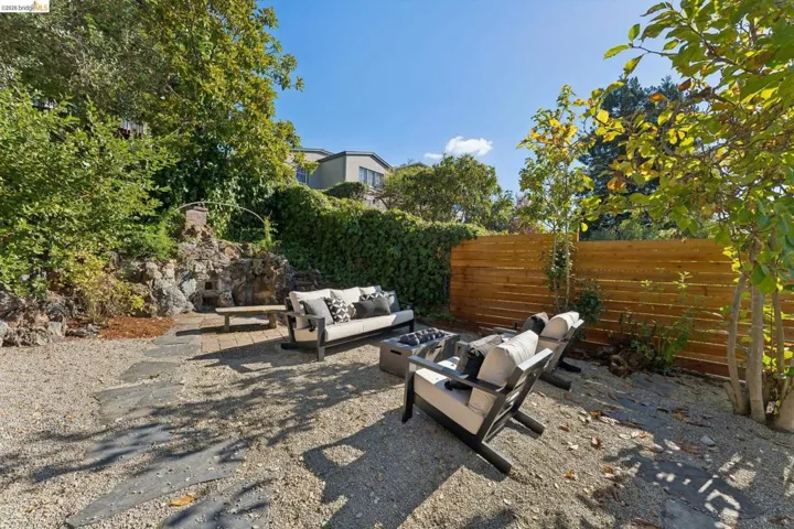 Landscaped backyard featuring a natural stone retaining wall, horizontal wood fencing, gravel ground cover, integrated stone seating, and mature trees